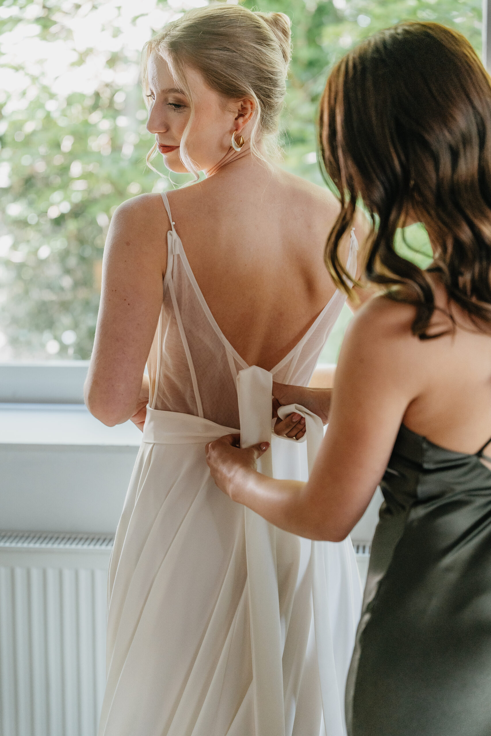 Trauzeugin hilft der Braut beim Anziehen und bindet ihr das Brautkleid zu